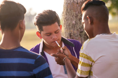 Youth culture young people group of male friends mixed race teen outdoor teenager in park. Hispanic kid smoking cigarette confident boy smoker. Health problems social issues.