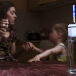 Drunk mother with alcoholic drink scolding her little son. Female alcoholism. Focus on bottle.